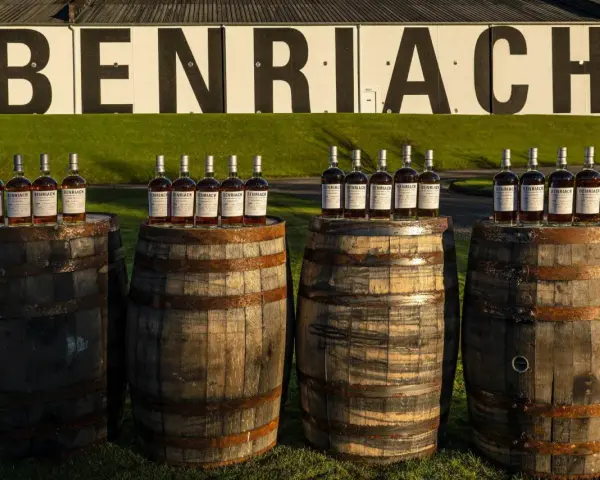 Butelki whisky Benriach stoją na beczkach, które czekają na dojrzewanie w pomieszczeniu.