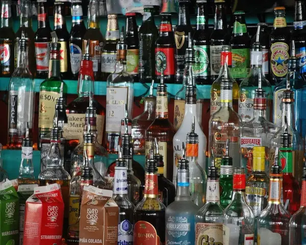 Różnorodne butelki alkoholi, w tym whisky, stoją na półce. Wskazówki, jak przechowywać whisky, mogą być przydatne przy tak bogatym asortymencie.