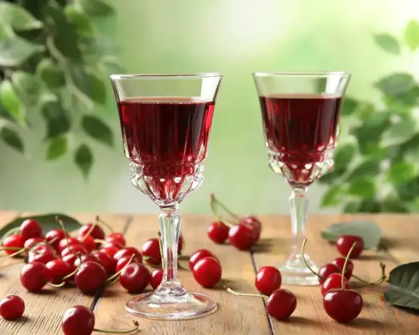 Dwa kieliszki z rubinową, szybką nalewką z wiśni na spirytusie, otoczone świeżymi wiśniami na drewnianym stole.