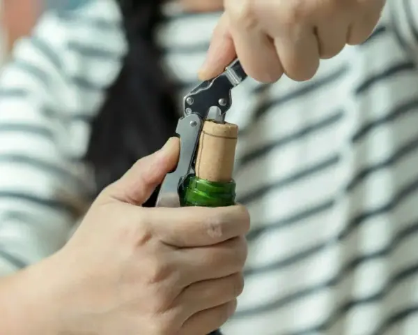 Ręce otwierają butelkę prosecco korkociągiem. Prosty sposób, jak otworzyć prosecco, by zacząć świętowanie.
