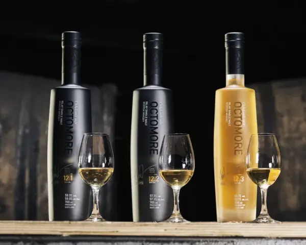 Trzy butelki Octomore, znanej z tego, że jest najbardziej dymna whisky, stoją obok kieliszków z bursztynowym płynem.