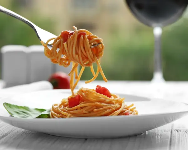 Widok na talerz spaghetti z sosem pomidorowym i listkiem bazylii. Widelec podnosi porcję makaronu. Idealne pytanie: jakie wino do bolognese?