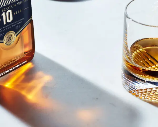 Butelka Ballantine's 10 Years Old i szklanka z bursztynowym płynem, przypominającym smak bourbona.
