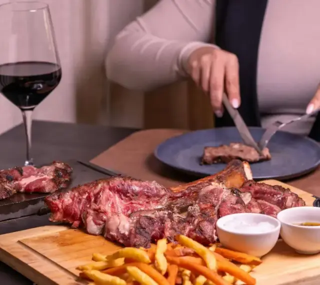 Idealne **jakie wino do wieprzowiny**? Czerwone wino i soczysta wieprzowina na desce, z frytkami i sosami.