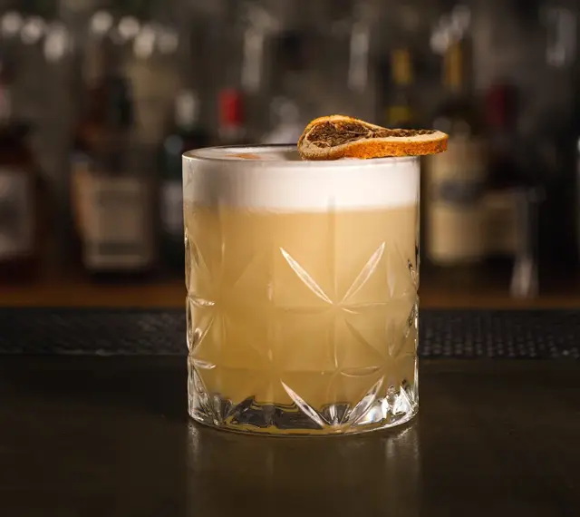 Klasyczny whisky sour z pianką i plasterkiem suszonej pomarańczy, gotowy do degustacji.