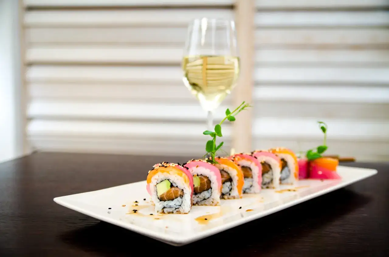 Kolorowe rolki sushi z łososiem i awokado, podane na białym talerzu, obok kieliszka białego wina. Idealne pytanie: jakie wino do sushi?