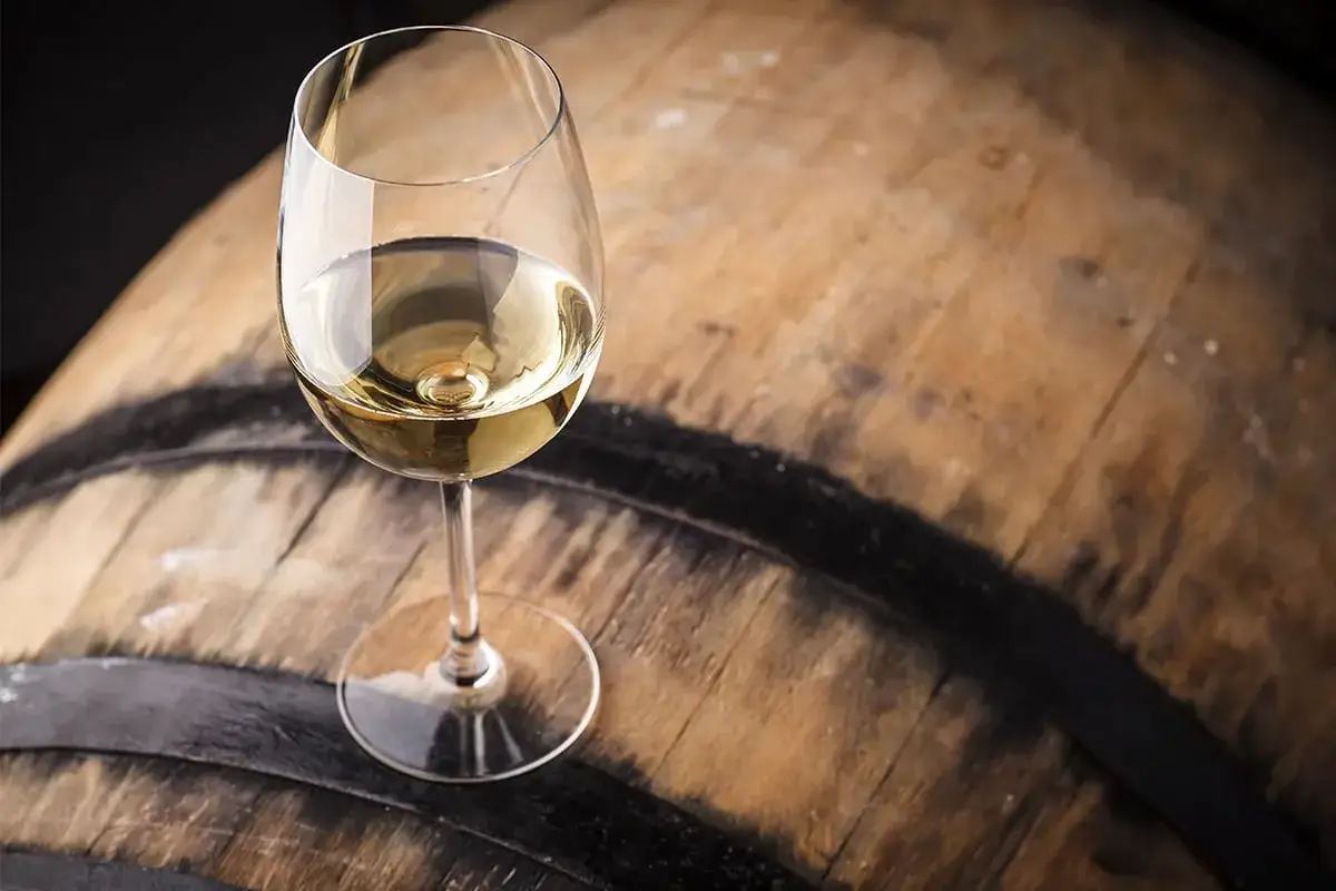 Szklanka pełna złotego chardonnay wina stoi na drewnianej beczce.