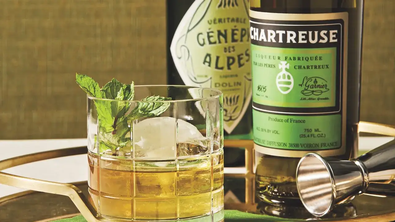 Szklanka z lodem i miętą, obok butelki Chartreuse. Jak pić ten likier?