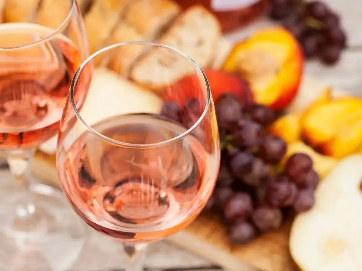 Idealny przepis na wino brzoskwiniowe: orzeźwiające różowe wino, winogrona, brzoskwinie i ser na desce.