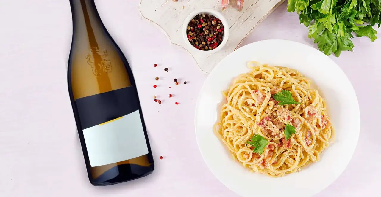 Idealne wino do carbonary? Obok butelki białego wina pyszna carbonara z parmezanem i pieprzem.