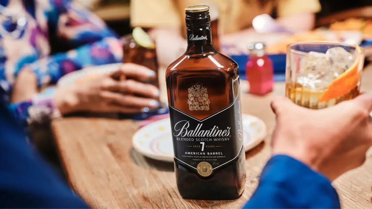 Butelka Ballantine's na stole, obok drinków. Idealnie pasuje do spotkań towarzyskich.