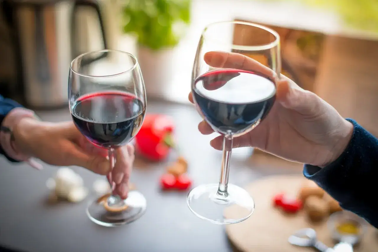 Dwie dłonie unoszą kieliszki z rubinowym, czerwonym winem, gotowe do toastu.