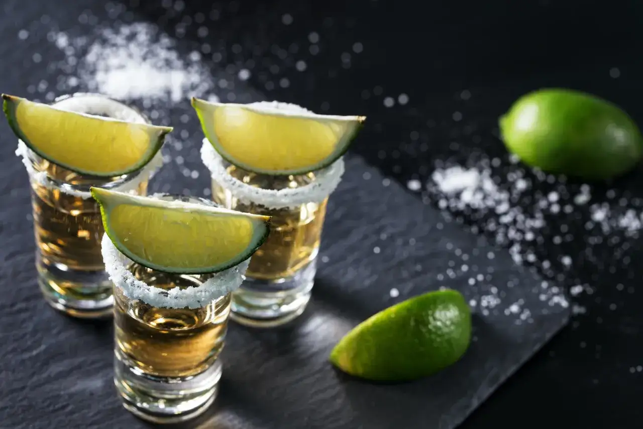 Złota tequila w kieliszkach z solą i limonką. Idealnie, by dowiedzieć się, jak pić tequilę gold.