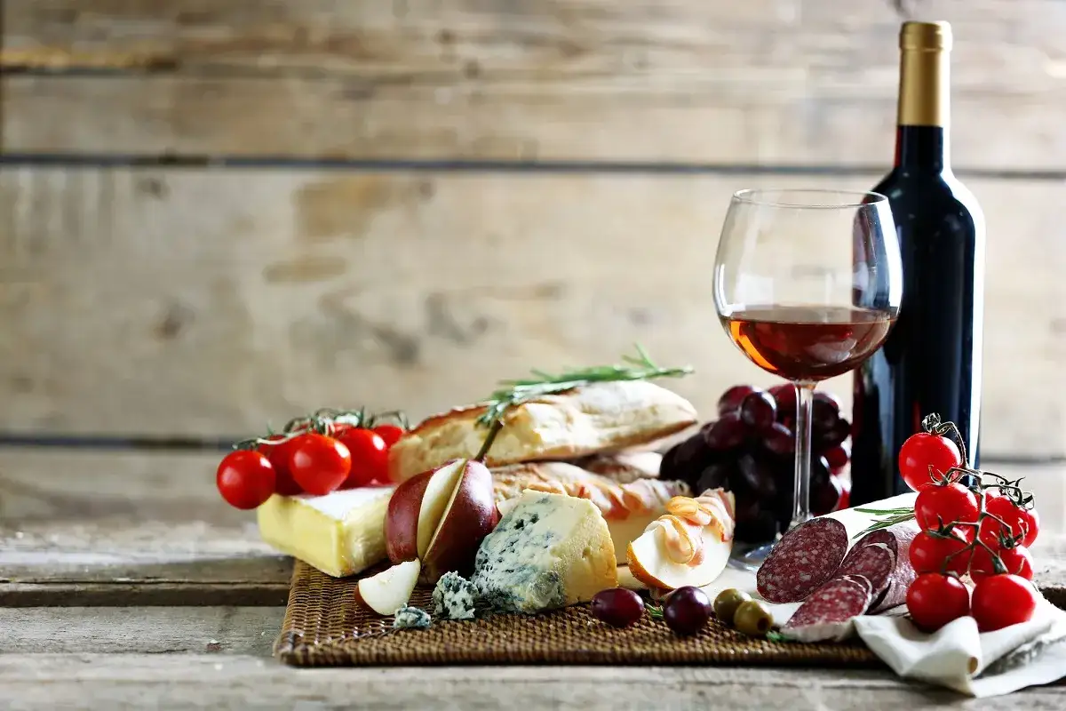 Kusi wino białe czy czerwone? Na stole ser, bagietka, winogrona, pomidorki i salami.