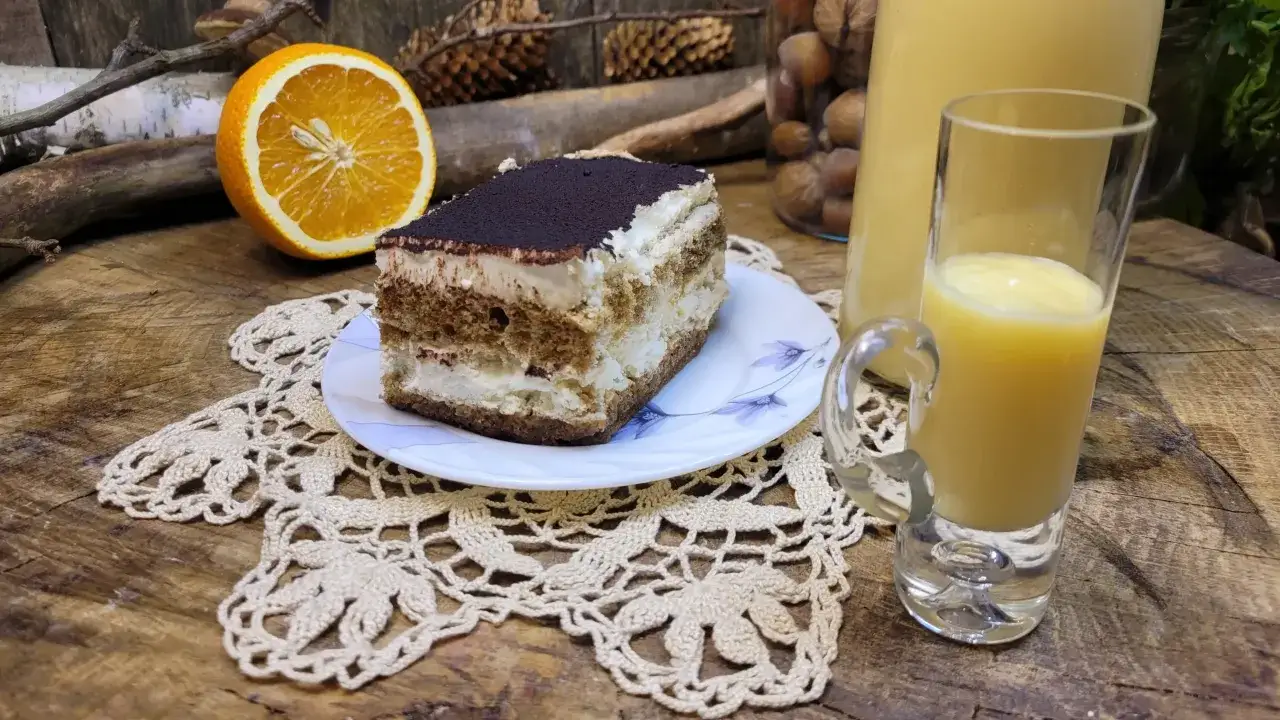 Słodki deser tiramisu i kieliszek likieru ze skórek pomarańczy, obok połówka pomarańczy.
