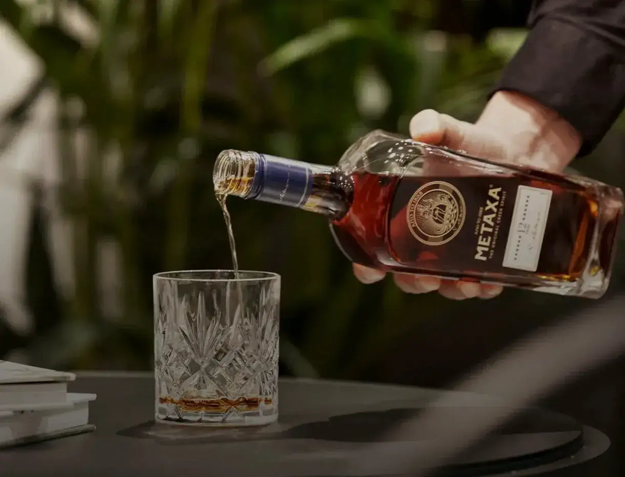Lejący się złocisty płyn z butelki Metaxa 12 gwiazdek do kryształowej szklanki. To właśnie metaxa co to za alkohol?