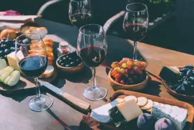 Degustacja merlot: jakie to wino? Kieliszki czerwonego wina, sery, winogrona, oliwki i pieczywo tworzą idealną kompozycję.