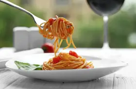 Widok na talerz spaghetti z sosem pomidorowym i listkiem bazylii. Widelec podnosi porcję makaronu. Idealne pytanie: jakie wino do bolognese?