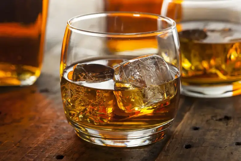 Szklanka złocistego trunku z lodem, obok butelki. Dylemat: whisky szkocka czy irlandzka?